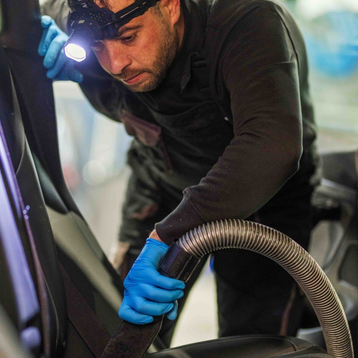 Medewerker reinigt het interieur van een auto met een zuigslang