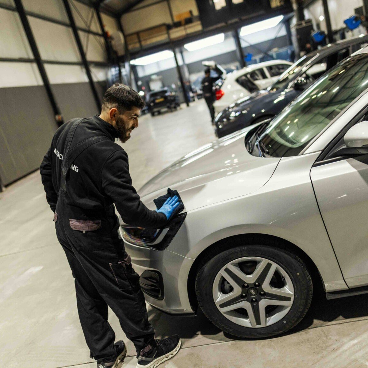 Medewerker reinigt de carrosserie van een zilveren auto tijdens een particuliere wasbeurt