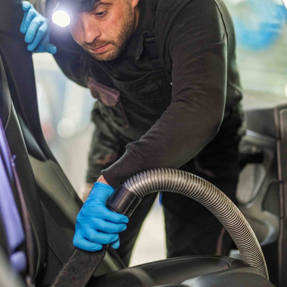 Medewerker stofzuigt het interieur van een auto met een zuigslang