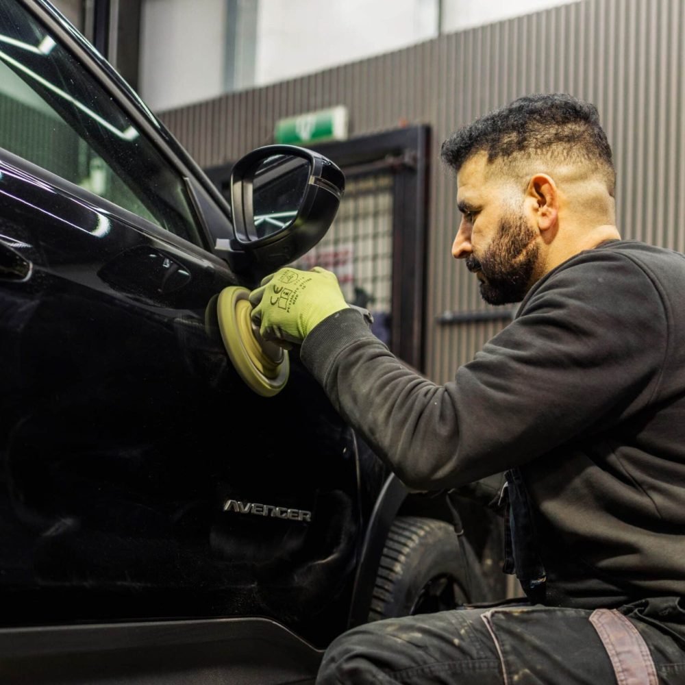 Medewerker polijst zwarte autolak met een polijstmachine